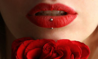 Lábios de mulher com piercing prateado e uma flor vermelha no queixo se avaliando se o batom vermelho atrai os homens.