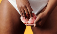 Mãos de mulher morena mexendo em fruta vermelha com suas cuecas brancas como pano de fundo, pensando nos benefícios da masturbação feminina.