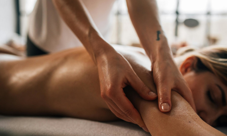 Mãos delicadas massageando ombro de mulher nua deitada durante brincadeiras eróticas.