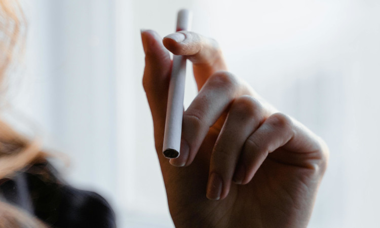 Mão de mulher segurando cigarro e pensando se o cigarro faz broxar.