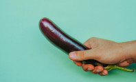Mão de homem segurando beringela pequena para mostrar como bater punheta sem gozar.