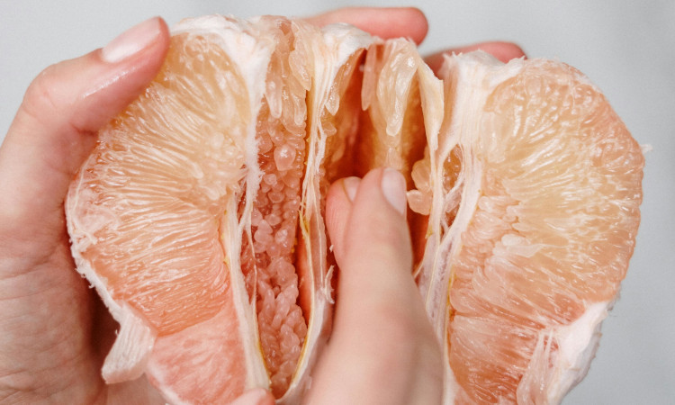 Mãos de mulher segurando toranja aberta a meio, mostrando como bater siririca sendo virgem.