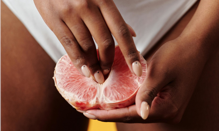 Mãos de mulher negra em cuecas brancas a mostrar como bater siririca numa toranja.