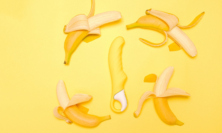 Imagem com fundo amarelo e 4 bananas espalhadas em círculo em torno de um brinquedo sexual para mostrar como bater uma boa punheta.