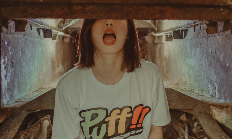 Mulher jovem de t-shirt, com rosto escondido, boca aberta e língua de fora se preparando para chupar as bolas.