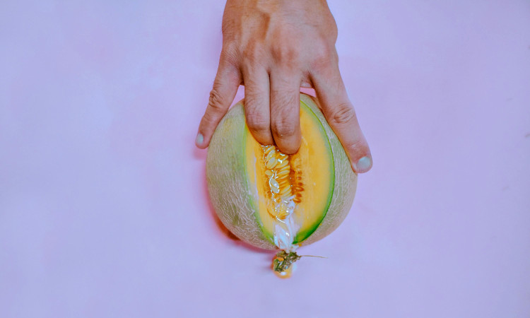 Mãos de homem com dedos dentro de meio melão simulando como dedar uma mulher.