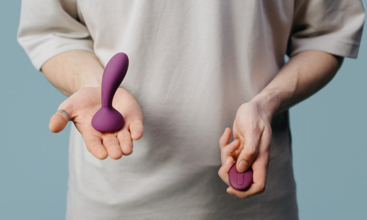 Tronco de homem com mãos segurando brinquedo sexual e o seu comando dando dicas de como estimular a próstata.