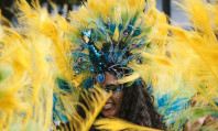 Mulher negra brasileira com seu rosto coberto de plumas amarelas pensando em como evitar dengue no Carnaval.