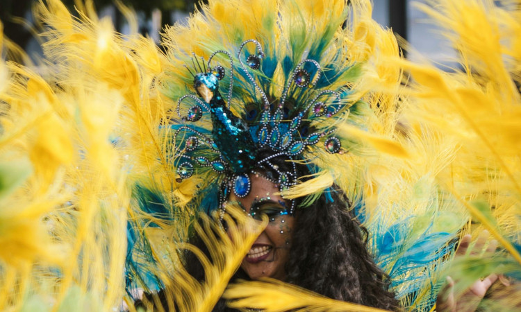 Mulher negra brasileira com seu rosto coberto de plumas amarelas pensando em como evitar dengue no Carnaval.