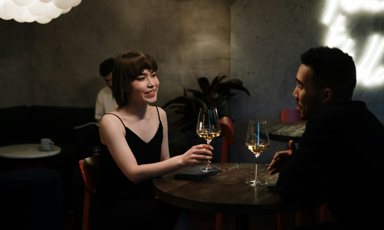 Casal de mulher de origem asiática e homem negro segurando copos durante jantar e pensando em como puxar assunto safado.