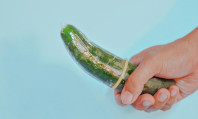Mão de homem a segurar pepino verde com um preservativo e a pensar em como saber o tamanho da camisinha.