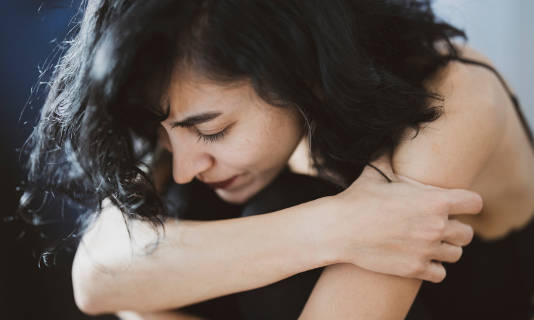 Mulher jovem de cabelo preto segurando seus joelhos por sentir enjoo depois do sexo.