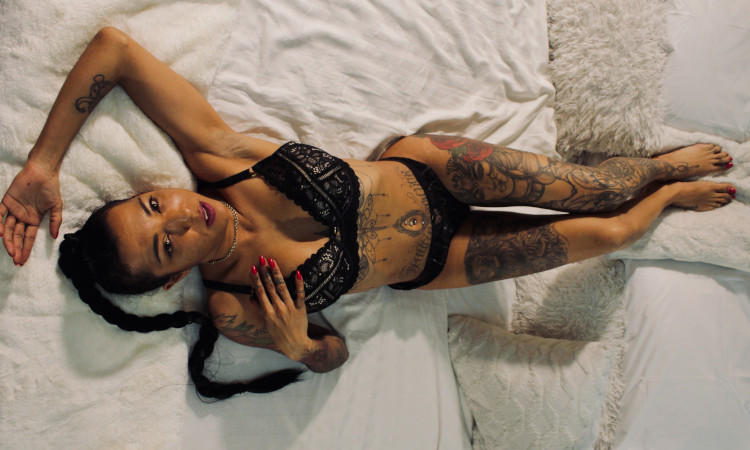 Mulher morena com tatuagens e piercings deitada na cama a ilustrar o que é estigmatofilia.
