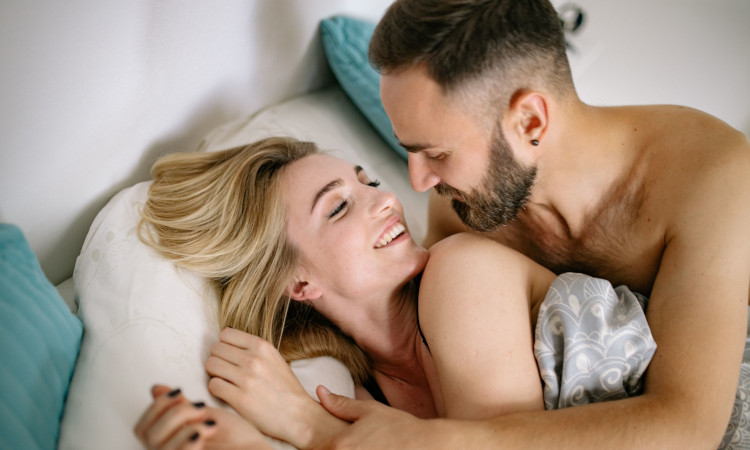 Homem e mulher sorrindo na cama, não sentindo falta de vontade de fazer sexo.