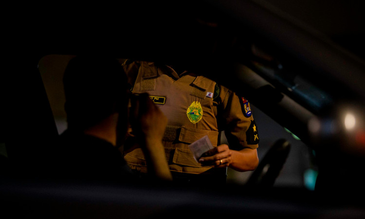 Tronco de policial, sem se ver seu rosto, pedindo documento a homem dentro de carro e explicando que fazer sexo na rua é crime.