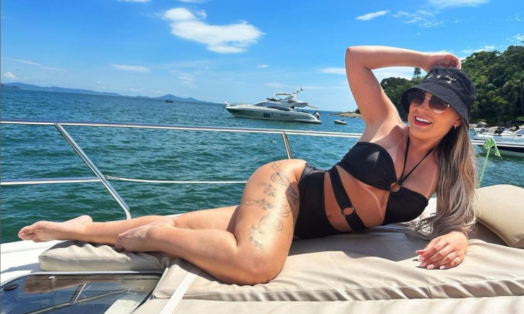 Andressa Urach em um iate com o mar em fundo, usando bikini e chapéu pretos e revelando uma das maiores bundas do Brasil.
