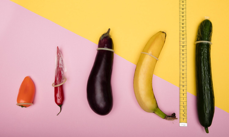 Frutas coloridas com fita métrica e preservativos em fundo rosa e amarelo ilustrativos dos maiores pênis.