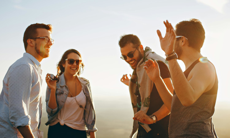 Quatro amigos (três homens e uma mulher) rindo ao pôr-do-sol durante perguntas para Eu Nunca quentes.