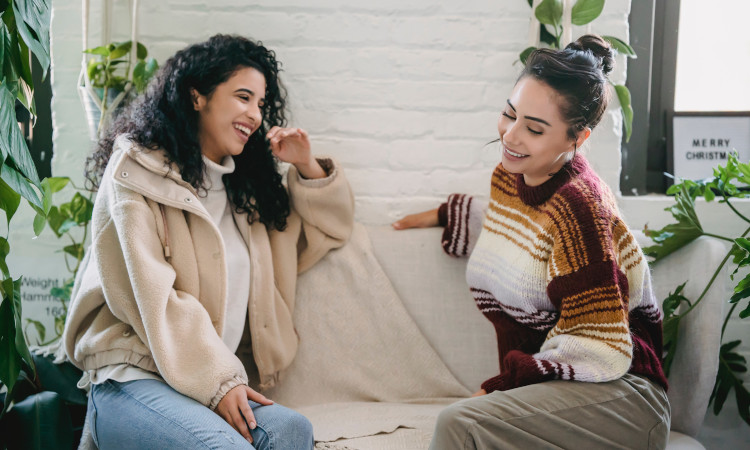 Duas mulheres conversando e sorrindo no sofá e falando de perguntas pesadas para o crush.