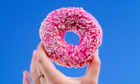 Mão segurando donut com cobertura rosa pensando sobre o que é sexo anal giratório.