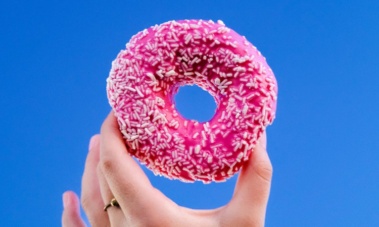 Mão segurando donut com cobertura rosa pensando sobre o que é sexo anal giratório.