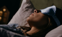 Rosto de mulher de venda azul a tapar os olhos e cabelos pretos, deitada na cama, a sonhar com sexo anal.