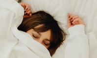 Mulher deitada na cama com lençóis brancos e olhos fechados a sonhar fazendo sexo com ex.