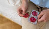 Mãos de mulher seguram vários tipos de camisinha de cor vermelha.