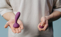 Tronco de figura masculina com camisola de manga curta bege segurando vibrador para homem roxo numa mão e um comando da mesma cor na outra.