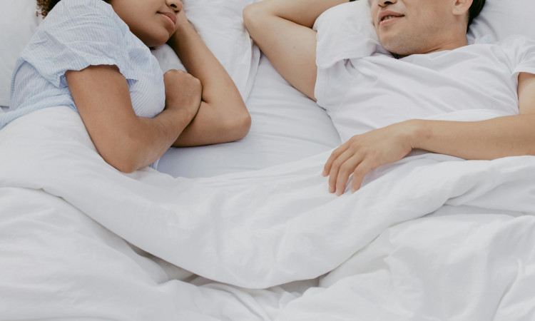 Casal de mulher morena e homem asiático conversando sobre polucao noturna na cama.